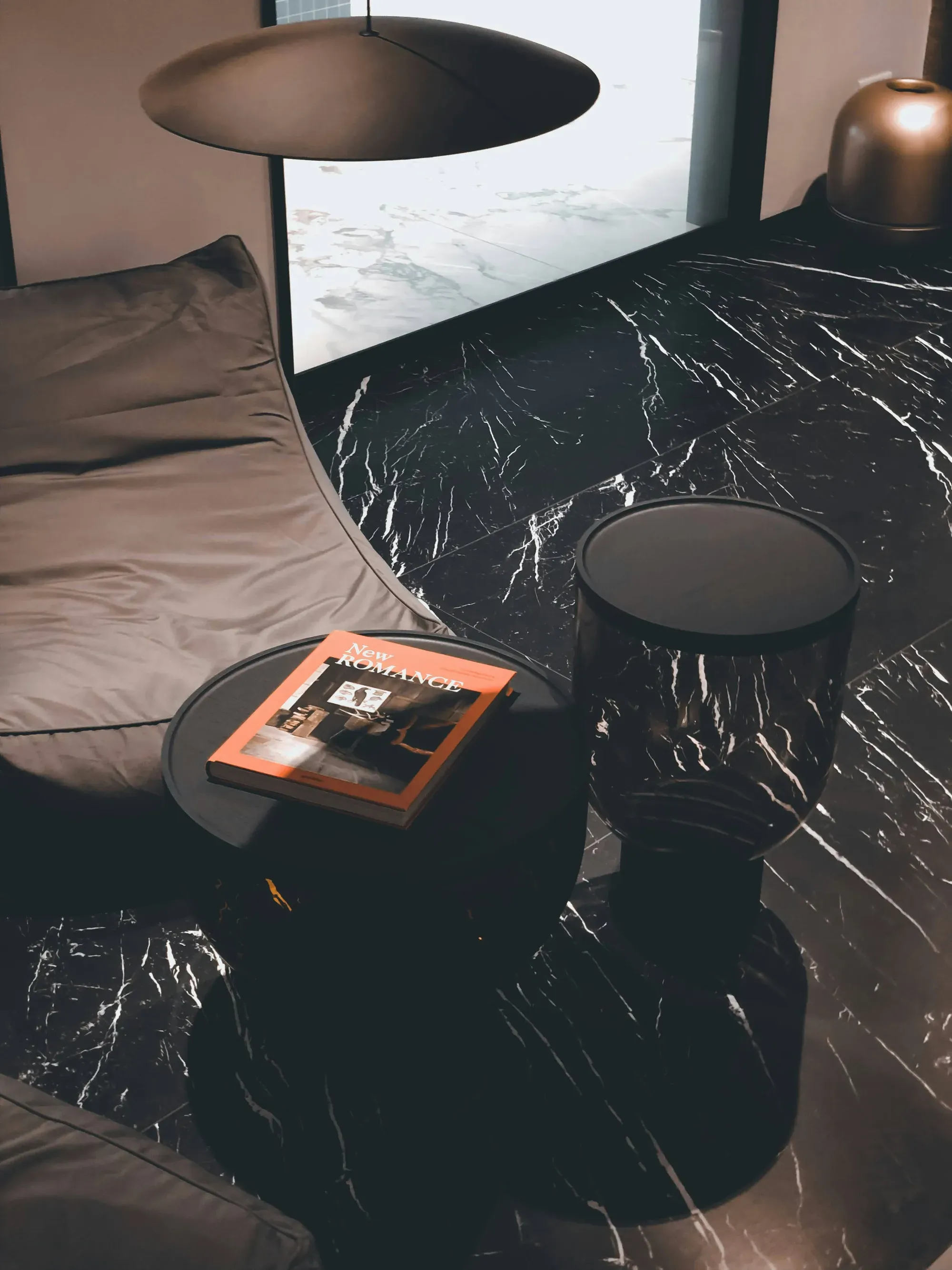 A cozy seating nook featuring a lounge chair, small side table with a book, and dark marble flooring.