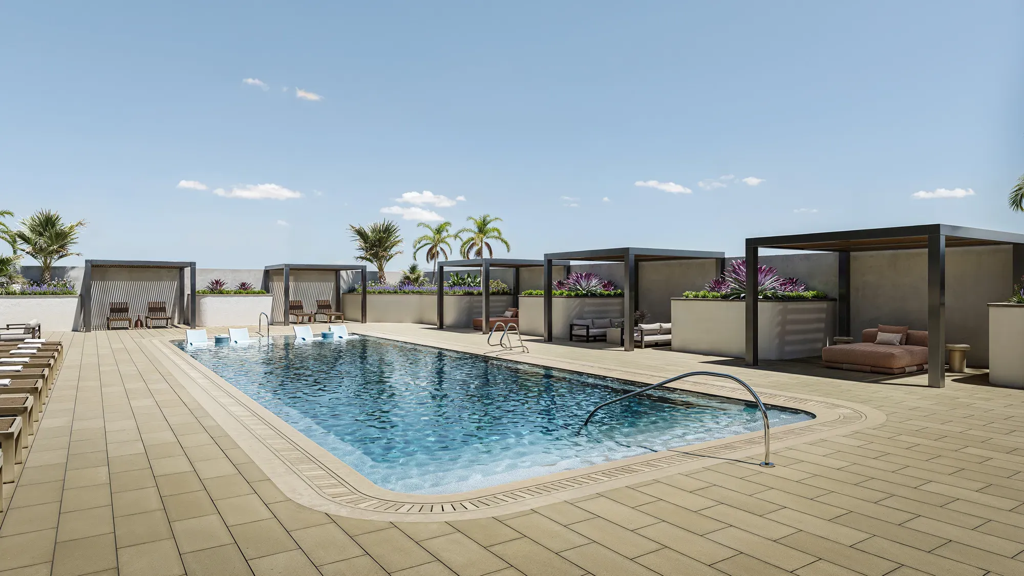 Swimming pool deck lined with shaded cabanas and lounge chairs.