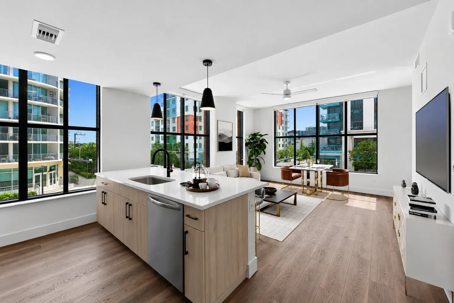 Open-concept modern living room and kitchen with large windows and light wood floors.