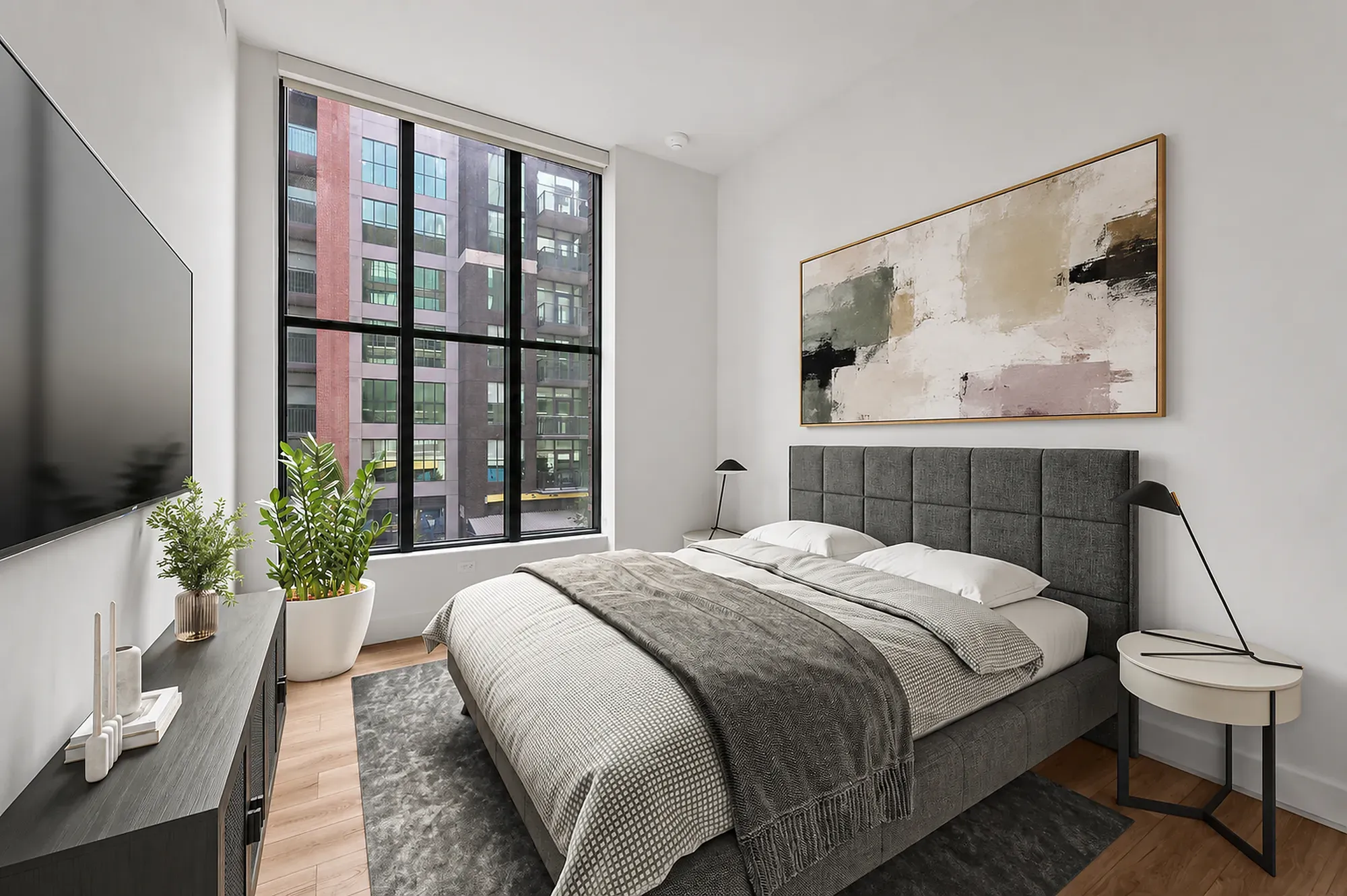 Modern apartment bedroom with a dark grey upholstered bed and large window.
