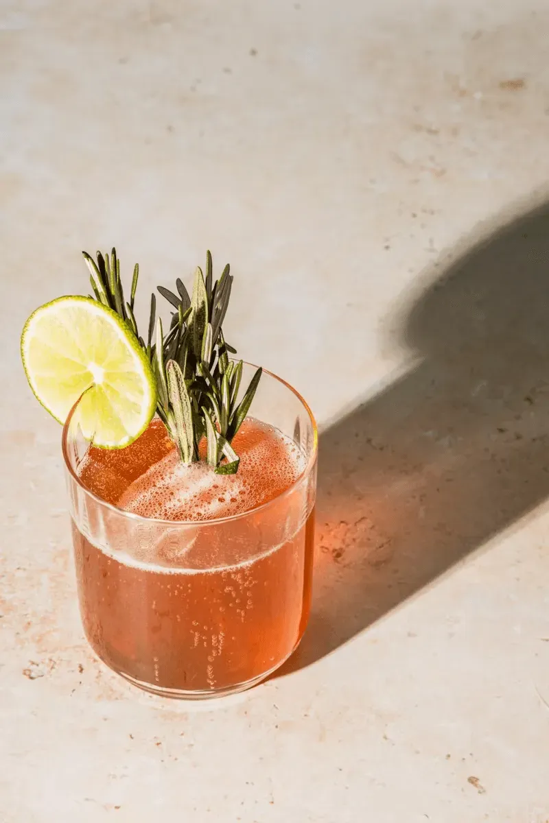 An iced craft cocktail garnished with a fresh lime wheel and a sprig of rosemary.