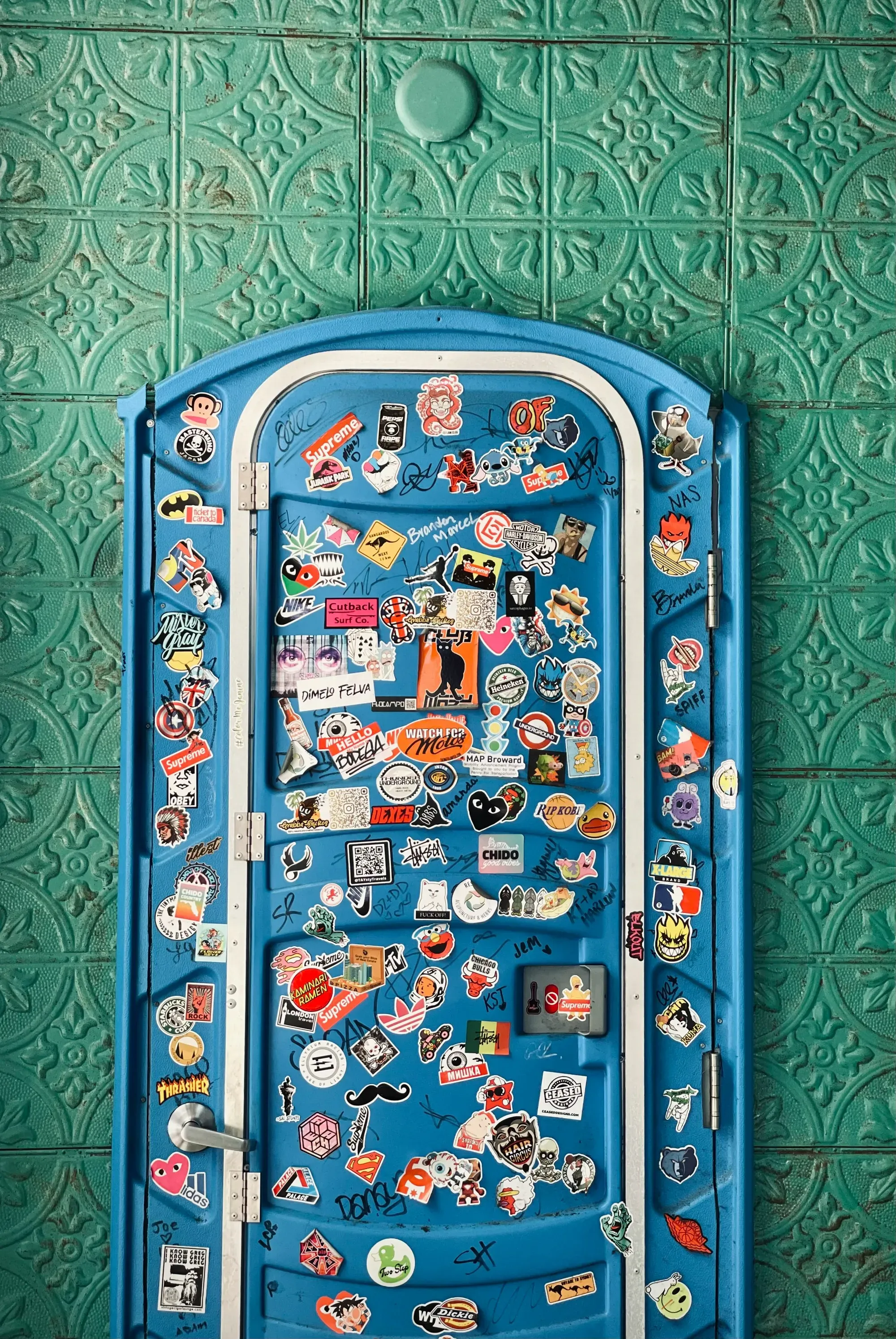 Close-up of a blue portable toilet door covered in a colorful collage of stickers.